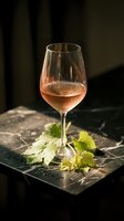 Elegant rose wine glass on dark marble surface with fresh grape leaves in moody atmospheric lighting for luxury dining and wine tasting experiences.