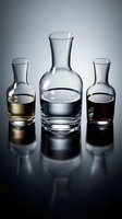 Three glass bottles and tumblers filled with different liquids including water, whiskey and wine against gray background with reflections.