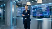 Professional businesswoman standing confidently in modern tech office with digital displays showing data analytics and machine learning interfaces.