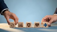 Healthcare professional arranging wooden blocks with medical icons including stethoscope, chart, shield, heartbeat and plus sign on blue background for insurance concept.
