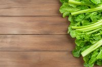 Fresh green celery stalks and leaves arranged on rustic wooden planks background, creating natural border composition for food photography and design.