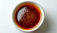 Red chili oil with crushed pepper flakes in white ceramic bowl on light background, top view close up of traditional Asian condiment for cooking and seasoning.