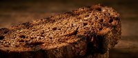 Slice of whole grain bread with seeds on rustic wooden surface, suitable for bakery, food, and culinary design projects.