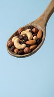 Wooden spoon filled with mixed nuts and dried fruits including cashews, almonds, walnuts and raisins on light blue background for healthy snacking concepts.
