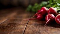 Fresh red radishes with green leaves on rustic wooden table background, selective focus with copy space for food photography and healthy eating concept.