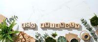 Eco friendly text on wooden letter cubes surrounded by green plants, moss, and craft paper on a white marble surface, sustainability concept.