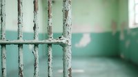 Prison cell bars with peeling paint against mint green wall, creating atmospheric mood of confinement and abandonment. Focus on weathered metal texture.