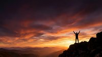 Person celebrating success on mountain peak during dramatic sunset with vibrant orange and purple sky over valley landscape for motivation and achievement concepts.