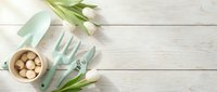 Mint green garden tools, white tulips, and bulbs on a light wooden surface, flat lay with copy space for spring gardening concepts.