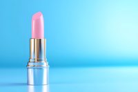 Pink lipstick with metallic silver case on bright blue background with copy space, minimalist cosmetic product photography for beauty and makeup advertising.