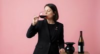 Professional businesswoman in black suit enjoying red wine tasting against pink background for lifestyle and corporate entertainment concepts.