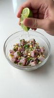 Hand squeezing fresh lime juice over mixed salad with ham, corn, and peas in glass bowl for cooking and food preparation.