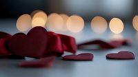 Red heart decorations with burgundy satin ribbon against blurred bokeh lights background create romantic Valentine's Day or wedding celebration atmosphere.