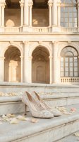 Elegant white lace bridal heels on marble steps with rose petals against classical architecture backdrop for wedding photography and romantic occasions.