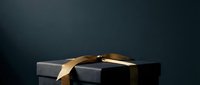 Black gift box with gold ribbon bow on dark background, luxury present for holidays, celebrations, and special occasions.