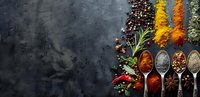 Aromatic spices and herbs in vintage spoons on dark background with copy space. Colorful seasoning border arrangement for culinary designs.