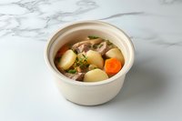 Hearty meat and potato soup with carrots and herbs in white ceramic bowl on marble background, homestyle comfort food served hot and fresh.