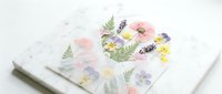 Pressed dried flowers arranged in a heart shape on white marble surface, soft pastel pink, purple and yellow blooms with fern leaves, romantic floral art.
