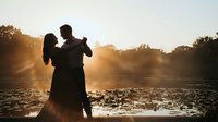 Romantic couple dancing together in silhouette against golden sunset light by river, intimate moment of love and connection in nature during golden hour.