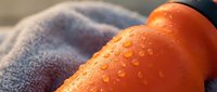 Ripe orange with water droplets on soft towel, fresh citrus fruit ready for juice or cooking applications.