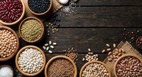 Assorted legumes and beans in wooden bowls on rustic dark table. Healthy protein sources including lentils, chickpeas, kidney beans for cooking and nutrition.