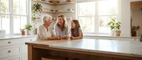 Mature Caucasian man and woman with adult daughter gathered at kitchen island, enjoying quality family time together in bright, modern home interior.