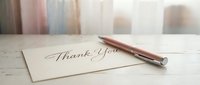 Elegant thank you card with calligraphy script on cream paper beside rose gold pen on wooden desk with soft natural lighting for gratitude messages.