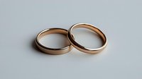 Two rose gold wedding bands on light background, minimalist composition showing classic plain metal rings symbolizing marriage and commitment.