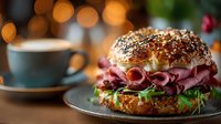 Gourmet bagel sandwich with pastrami, arugula, and cream cheese on a dark plate with coffee cup and warm bokeh background.