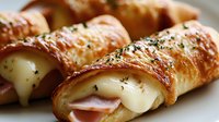 Freshly baked croissant rolls filled with melted cheese and ham, sprinkled with herbs on white plate, ready to serve for breakfast or brunch.