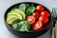 Fresh healthy bowl with sliced avocado, cherry tomatoes and spinach leaves on gray background. Nutritious vegetarian meal for diet and wellness lifestyle.