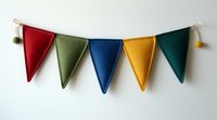 Colorful felt pennant banner with five triangular flags in red, olive green, navy blue, yellow and forest green, decorated with pom-pom tassels on white background.