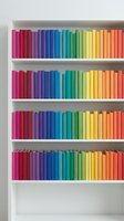 Colorful books arranged by rainbow spectrum on white bookshelf creating organized library display for interior design and educational concepts.