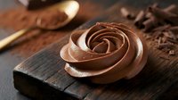 Chocolate rose decoration on wooden cutting board with cocoa powder and kitchen utensils for pastry making and dessert preparation.