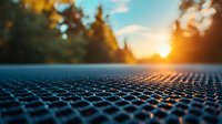 Close-up view of solar panel texture at sunset with golden sun rays filtering through pine trees, creating dramatic lighting and bokeh effect on photovoltaic surface.