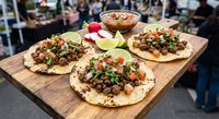 Authentic Mexican street tacos with fresh cilantro, onions and salsa served on corn tortillas at bustling outdoor food market for culinary dining experiences.