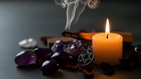Burning candle with purple amethyst crystals and smoking incense creating mystical atmosphere for meditation, healing rituals, and spiritual wellness practices.