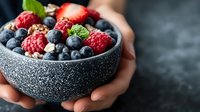Fresh mixed berries with granola in stone bowl against dark background, selective focus on ripe raspberries, blueberries and mint leaves, healthy breakfast concept.
