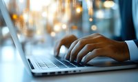 Close-up of African American male hands typing on laptop keyboard in office environment with soft bokeh lights and window reflections in background.