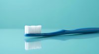 Blue toothbrush with white bristles on turquoise background with reflection. Dental hygiene and oral care concept for healthcare and wellness designs.