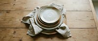 Stacked ceramic bowls and plates with linen napkin on wooden table surface for dining and tableware design projects.