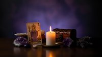 Mystical tarot card reading setup with burning candle, amethyst crystals, and lavender sprigs creating atmospheric fortune telling scene.