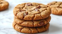 Stack of freshly baked chocolate chip cookies with crispy edges and gooey centers on white marble background, close-up view showing texture and melted chips.