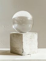 Clear glass sphere on concrete cube pedestal against neutral background, minimalist composition with natural light and shadow play creating artistic still life.