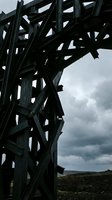 Dark industrial steel framework structure against cloudy sky, showcasing geometric metal beams and architectural engineering design for construction and industrial projects.