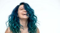 Young woman with vibrant teal blue hair laughing joyfully against white background. Expressive portrait showing happiness and positive emotions for lifestyle content.
