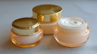 Luxury skincare cream jars with gold lids and peach-tinted glass containers, showcasing different textures of cosmetic products for premium beauty routines.