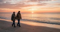 Two people walking on beach at sunset with golden sky and ocean waves creating romantic peaceful atmosphere for travel and leisure concepts.