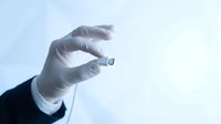 Scientist or medical professional wearing white latex gloves holding small microchip or computer processor against light background for technology research.