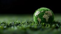 Green globe made of natural materials resting on fresh grass against dark background, representing environmental conservation and sustainable earth concept.